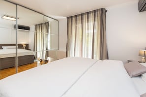 Een hotelkamer met een groot bed, een nachtkastje met een lamp, een spiegel en uitzicht op het landschap door dunne gordijnen.