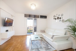 Un salon moderne avec un canapé blanc, un téléviseur à écran plat et un plancher en bois.
