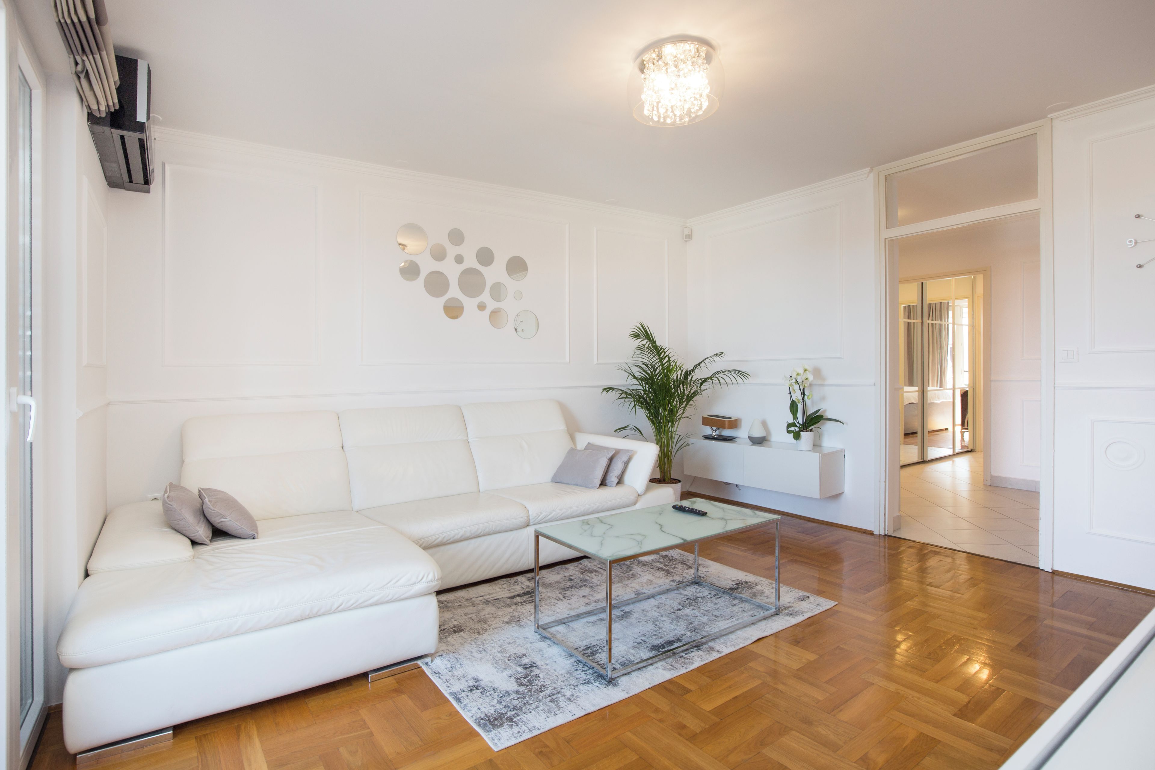 A modern living room with a white sofa, a glass coffee table, and a decorative wall with circular mirrors.