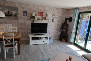 A living room with a television, a fireplace, a dining table with chairs, and a window with curtains. - Vacation home for up to 5 people—non-refundable, no pets allowed, no free cancellation (Boltenhagen)