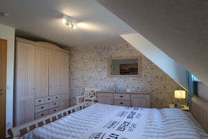A bedroom with a bed, a wardrobe, a desk, a chair, and a brick-patterned wall. - Vacation home for up to 5 people—non-refundable, no pets allowed, no free cancellation (Boltenhagen)