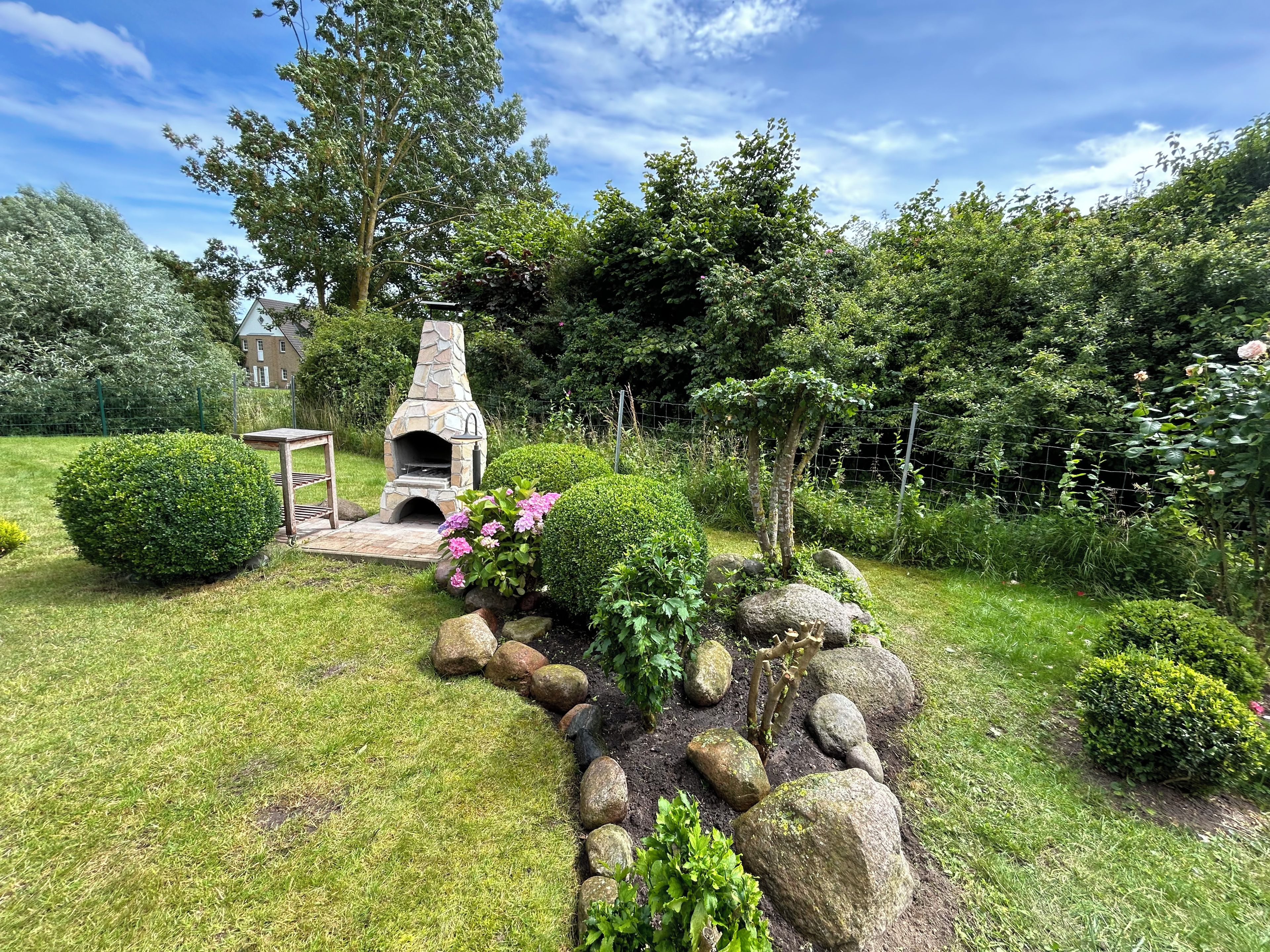 A stone-built outdoor fireplace surrounded by well-maintained garden beds and a variety of shrubs.