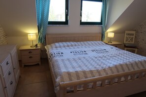 Une chambre à coucher avec un lit, deux tables de chevet avec des lampes, une commode et une fenêtre avec des rideaux.