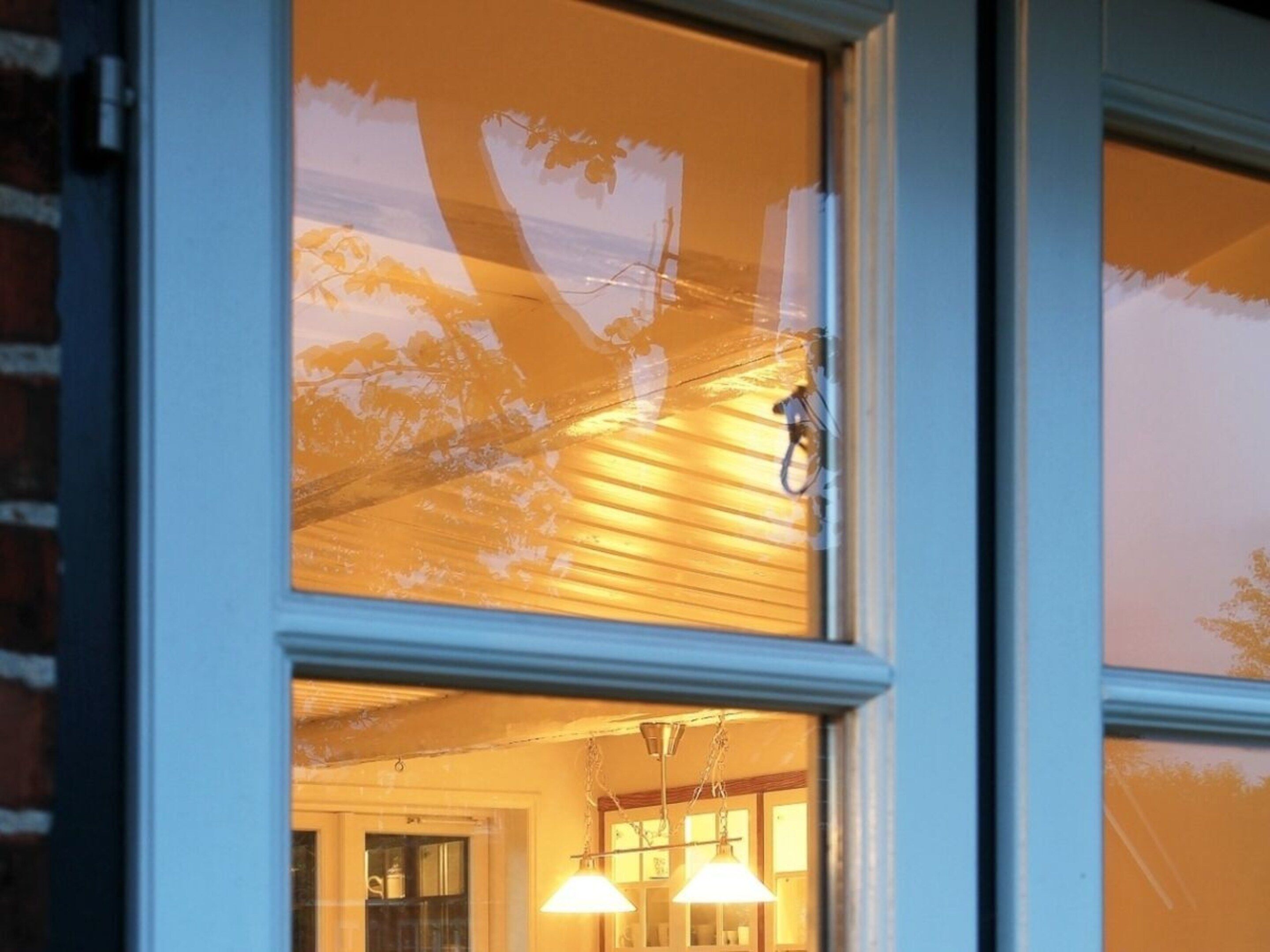 A window with a view of a building's interior, including a door and a hanging light fixture.