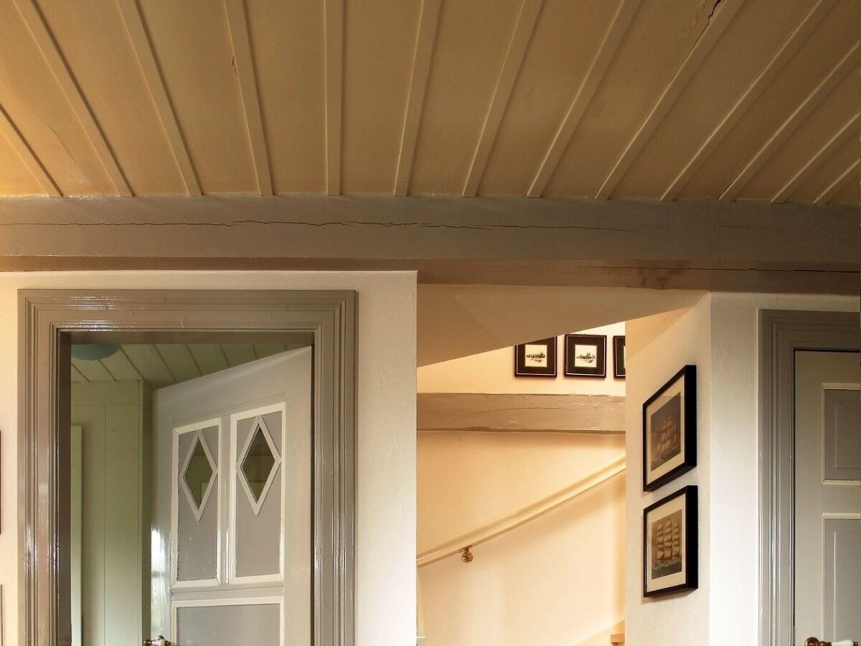 A hallway with a wooden ceiling, a door with diamond-shaped glass panels, and framed pictures on the wall.