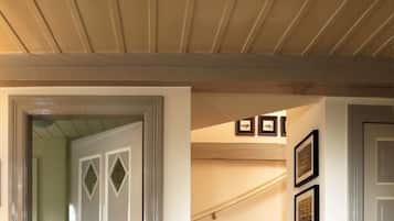 A hallway with a wooden ceiling, a door with diamond-shaped glass panels, and framed pictures on the wall.