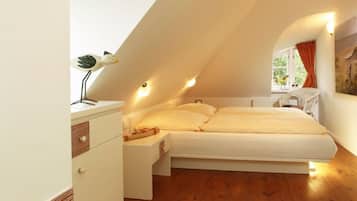 A bedroom with a sloped ceiling, a bed with white bedding, a bedside table with a lamp, and a window with curtains.