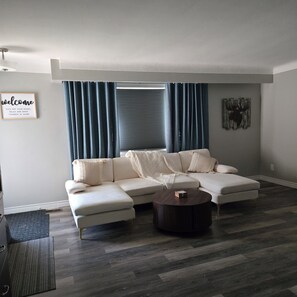 Een moderne woonkamer met een hoekbank, een salontafel en een raam met gordijnen.