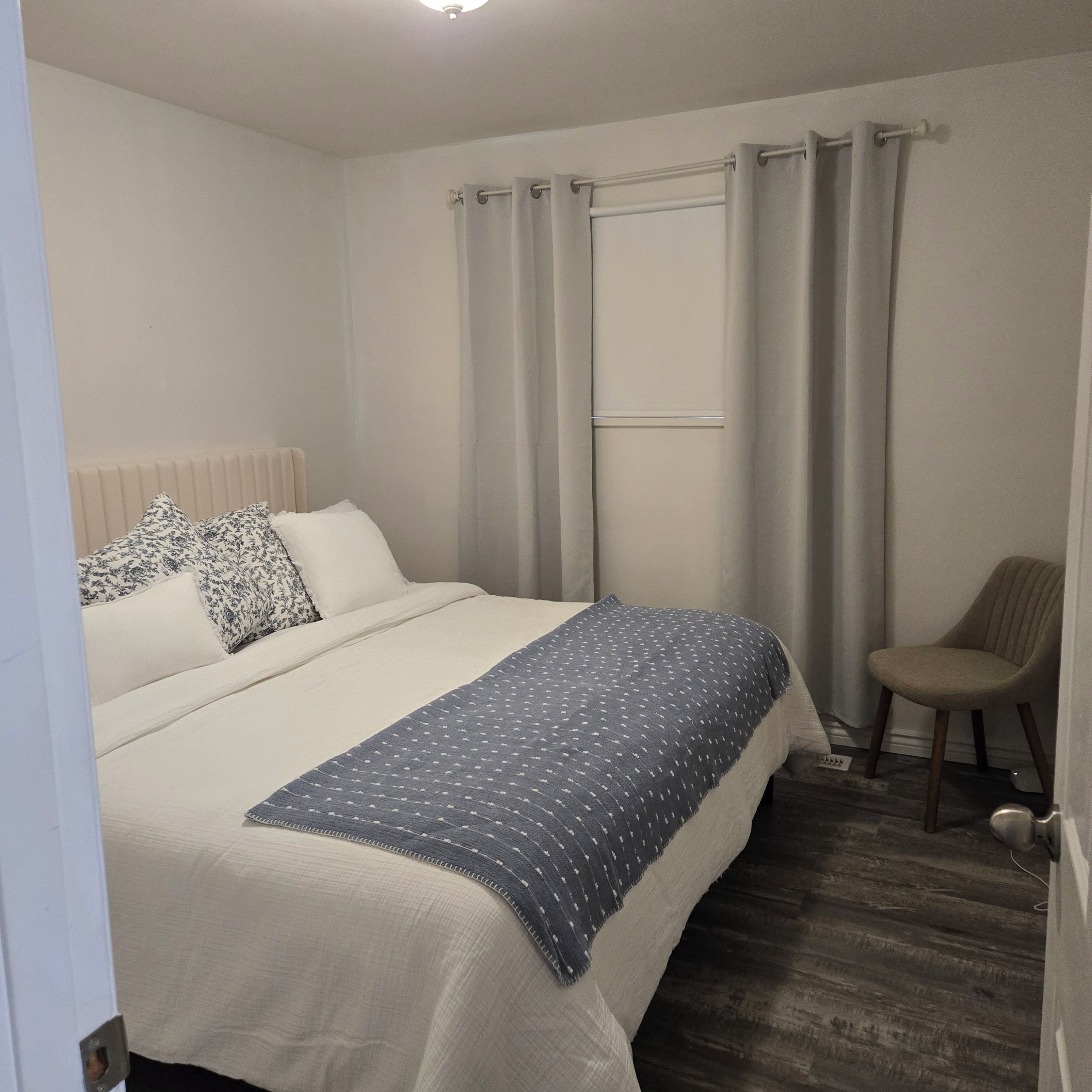 Une chambre à coucher avec un lit, une chaise, une fenêtre avec des rideaux et un radiateur.