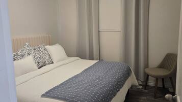 Une chambre à coucher avec un lit, une chaise, une fenêtre avec des rideaux et un radiateur.
