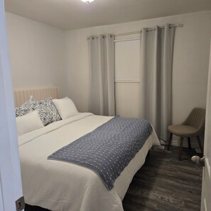 Een slaapkamer met een bed, een stoel, een raam met gordijnen en een radiator.