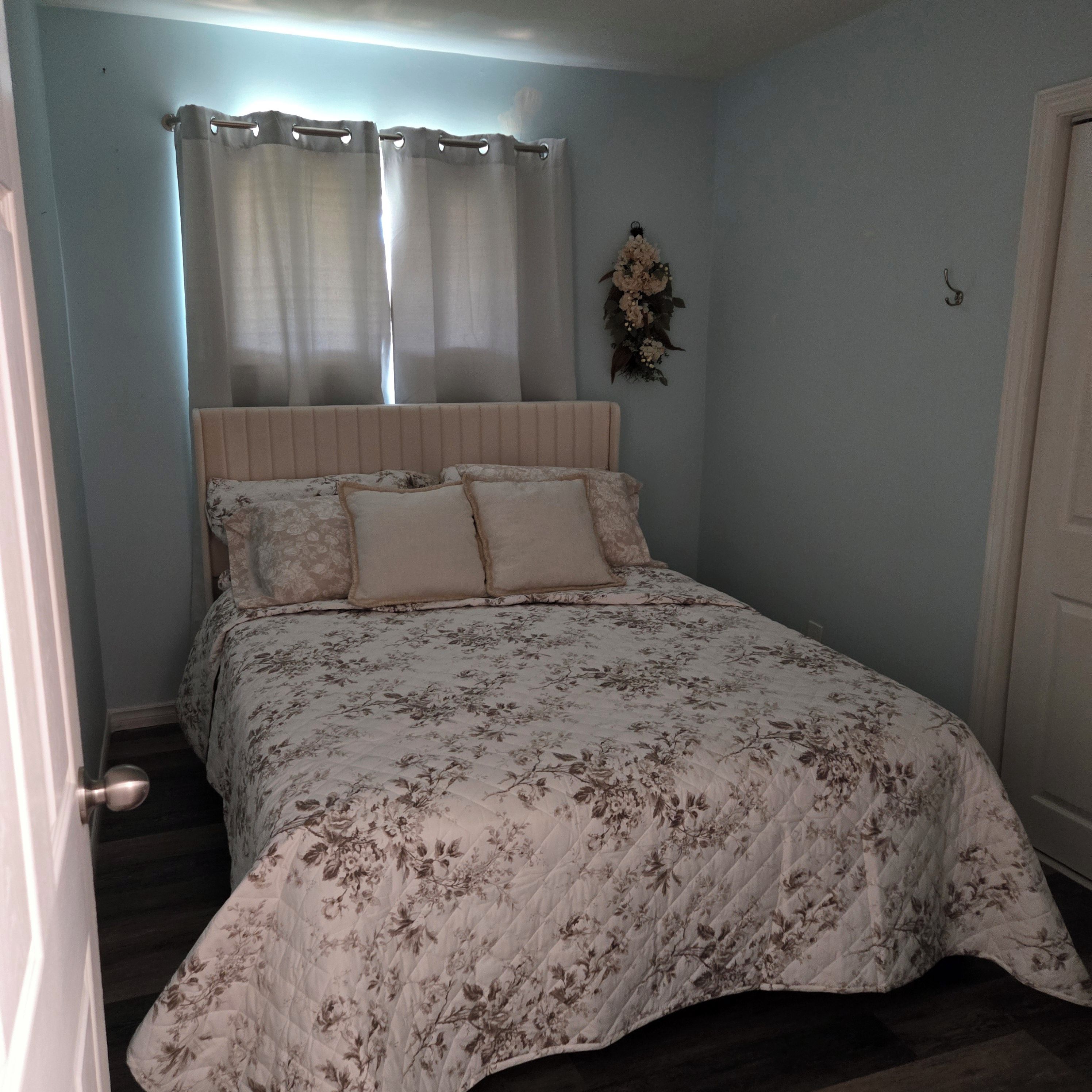 A bedroom with a bed, curtains, a floral bedspread, and a wall-mounted decoration.