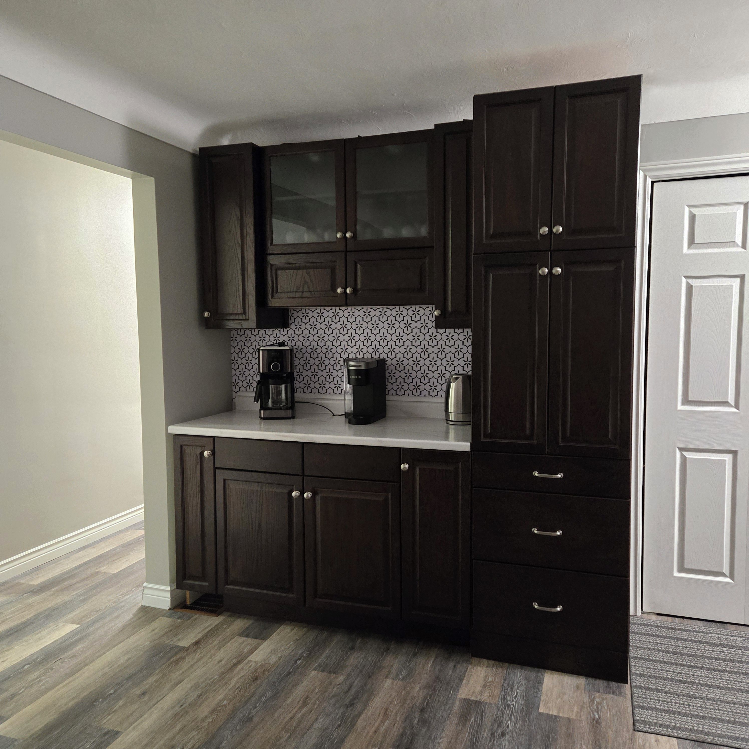 A kitchen with dark wood cabinets, a white countertop, and a patterned backsplash.