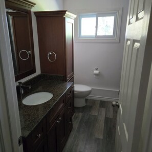 Een badkamer met een wastafel, spiegel, toilet en raam.