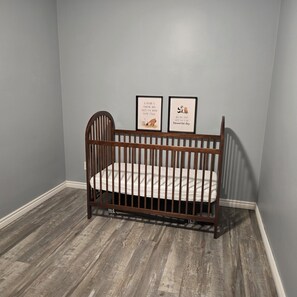 A wooden crib in a room with grey walls and wooden flooring.