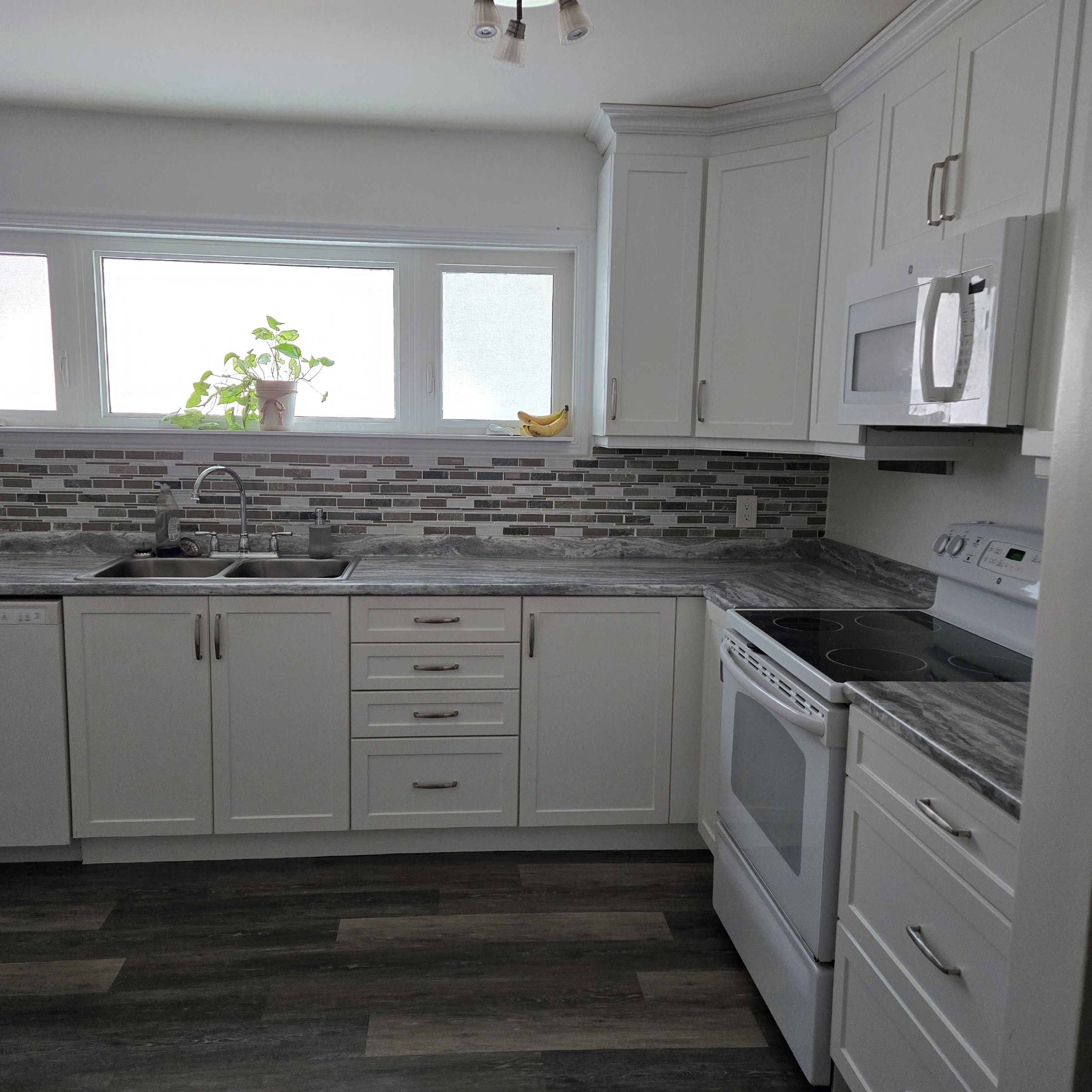 A kitchen with white cabinets, a sink, a stove, and a microwave.