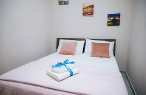 A neatly made bed with a folded white towel and a blue ribbon, a white wall with two framed pictures, and a plain white ceiling. - Casillo House Vacation Rental (Napoli)