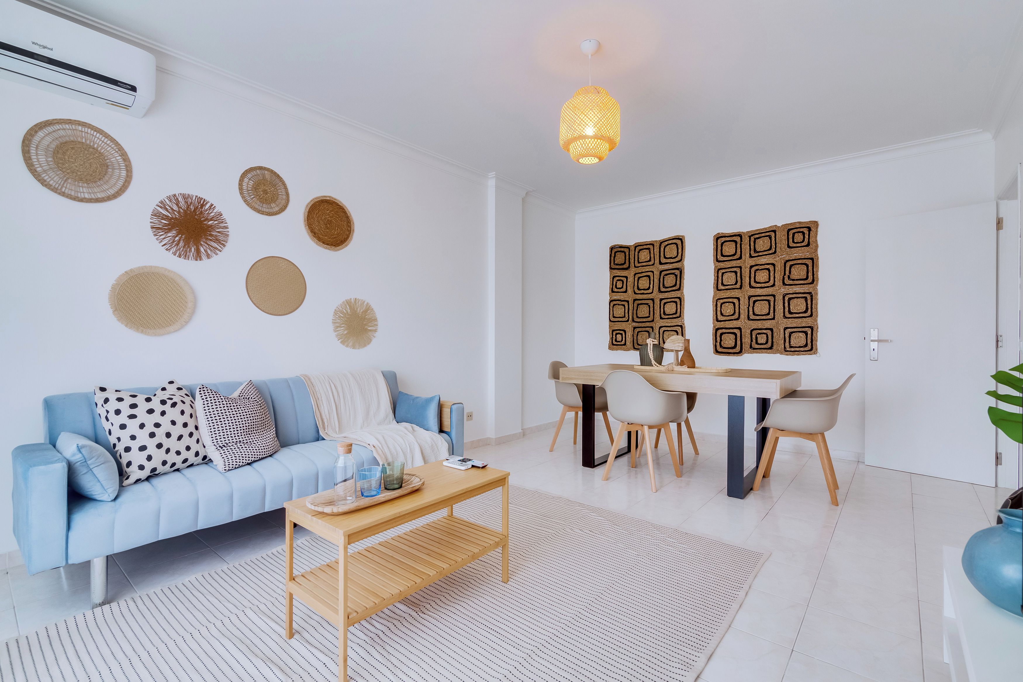 A modern living room with a blue sofa, a wooden coffee table, and a dining area with a white table and chairs.