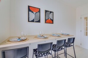 A dining area with a long table, four chairs, and two framed artworks on the wall. - Brisa Algarvia 2: A Cozy Apartment in Faro (Faro)