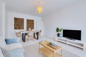 A modern living room with a sofa, coffee table, TV, and a dining area with chairs and a table. - Brisa Algarvia 2: A Cozy Apartment in Faro (Faro)