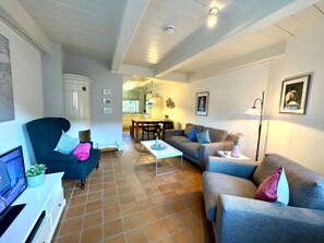 A living room with a sofa, armchair, and a TV on a stand. - Holiday Apartment With 1 Bedroom (Borgsum)