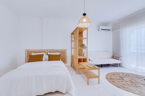A modern bedroom with a bed, a wooden nightstand, a white sofa, and a large window. - Brisa Algarvia 1 Family Apartment in Faro (Faro)