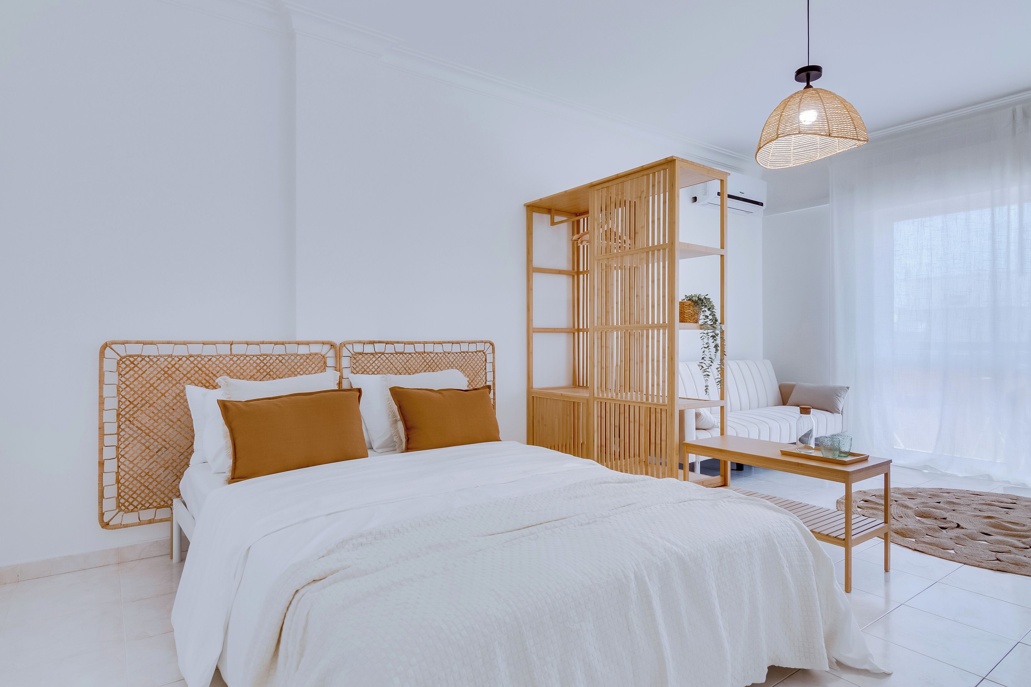 A bedroom with a bed, a wooden headboard, a nightstand, a hanging light fixture, and a window with sheer curtains.