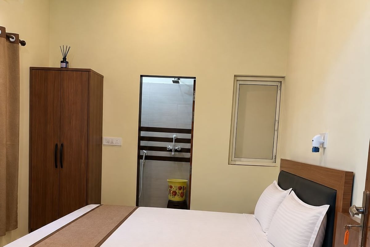 A hotel room with a wooden bed, a small bedside table, a wardrobe, a mirror, and a bathroom with a shower.
