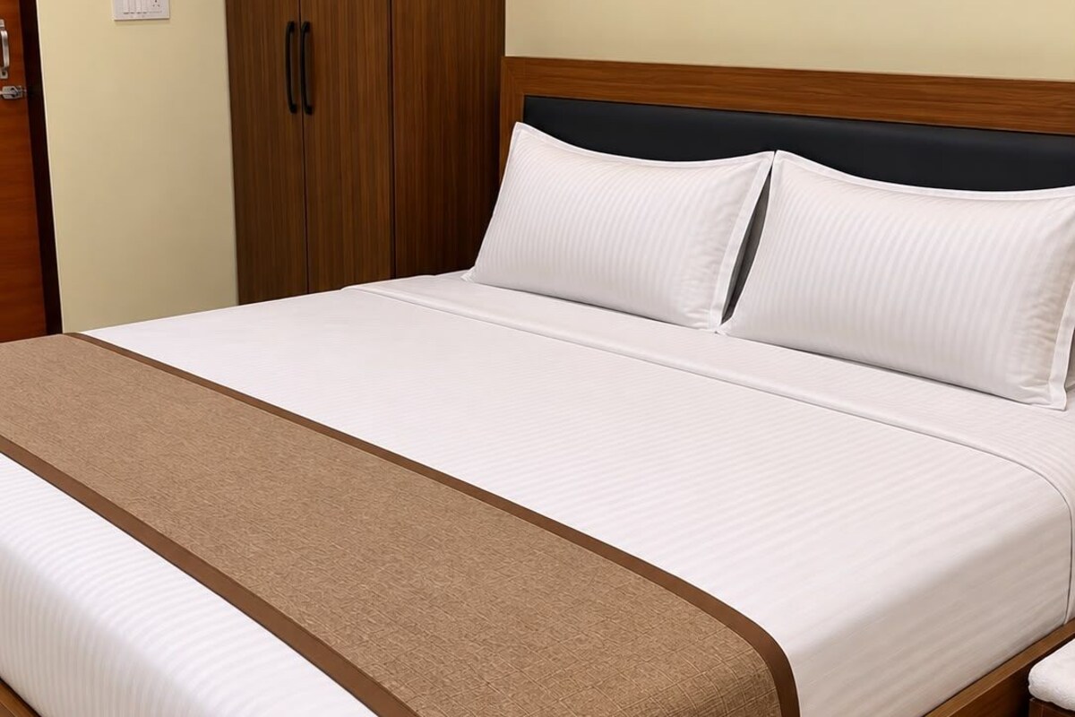 A neatly made bed with a wooden frame, white bedding, and a brown accent.