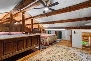 Een ruime zolderkamer met een groot bed, een plafondventilator en uitzicht op het landschap door een raam.