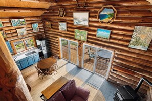Ein rustikales Blockhaus-Interieur mit Essbereich, Küche und großem Fenster mit Blick auf einen Garten.