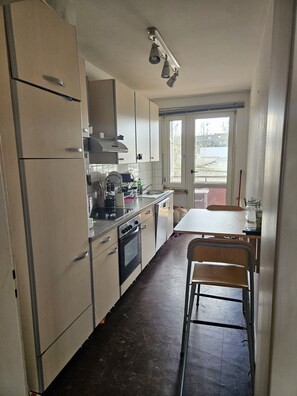 A kitchen with a refrigerator, stove, sink, and a dining area with a table and chairs. - Cozy apartment in the heart of Essen's Rüttenscheid neighborhood (Essen)