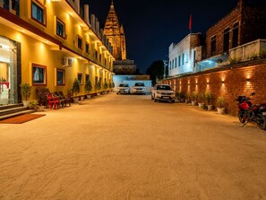 A hotel courtyard with a paved area, several parked cars, and a prominent building with a spire in the background. - Hotel Vaishnavi Grand 200 m 80 Ghat (Varanasi)