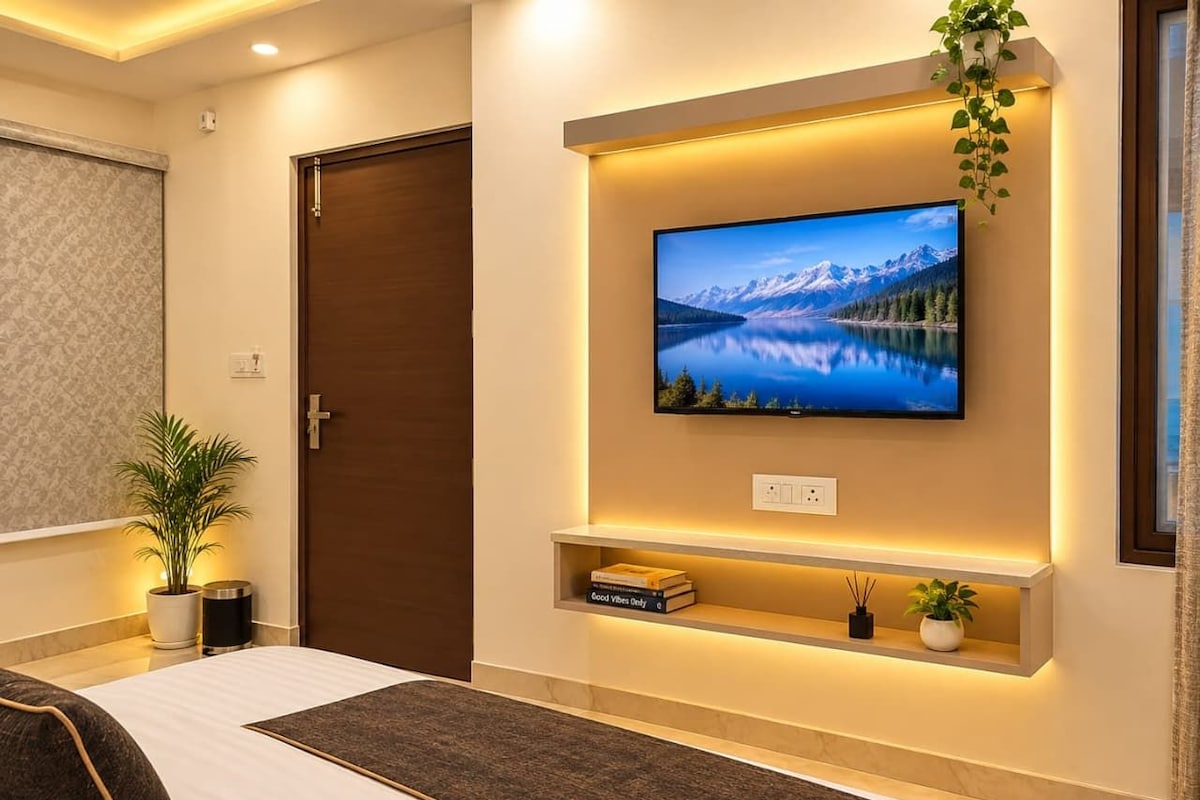 A modern bedroom with a large bed, a mounted TV, and a bedside table with a plant and books.