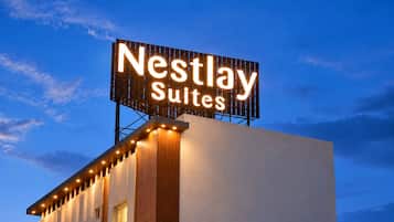 A building with a large illuminated sign reading 'Nestlay Suites' against a twilight sky.