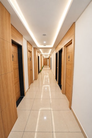 A hotel hallway with wooden doors, a tiled floor, and recessed lighting.