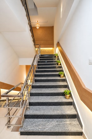 A modern staircase with a metal handrail, black steps, and potted plants at the landing. - Nestlay Suites Tirupati (Renigunta)