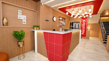 A hotel reception area with a modern design, featuring a red and white reception desk, a clock, and a staircase.