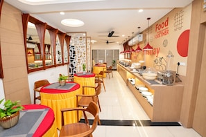 A restaurant with round tables, chairs, and a counter with food items. - Nestlay Suites Tirupati (Renigunta)