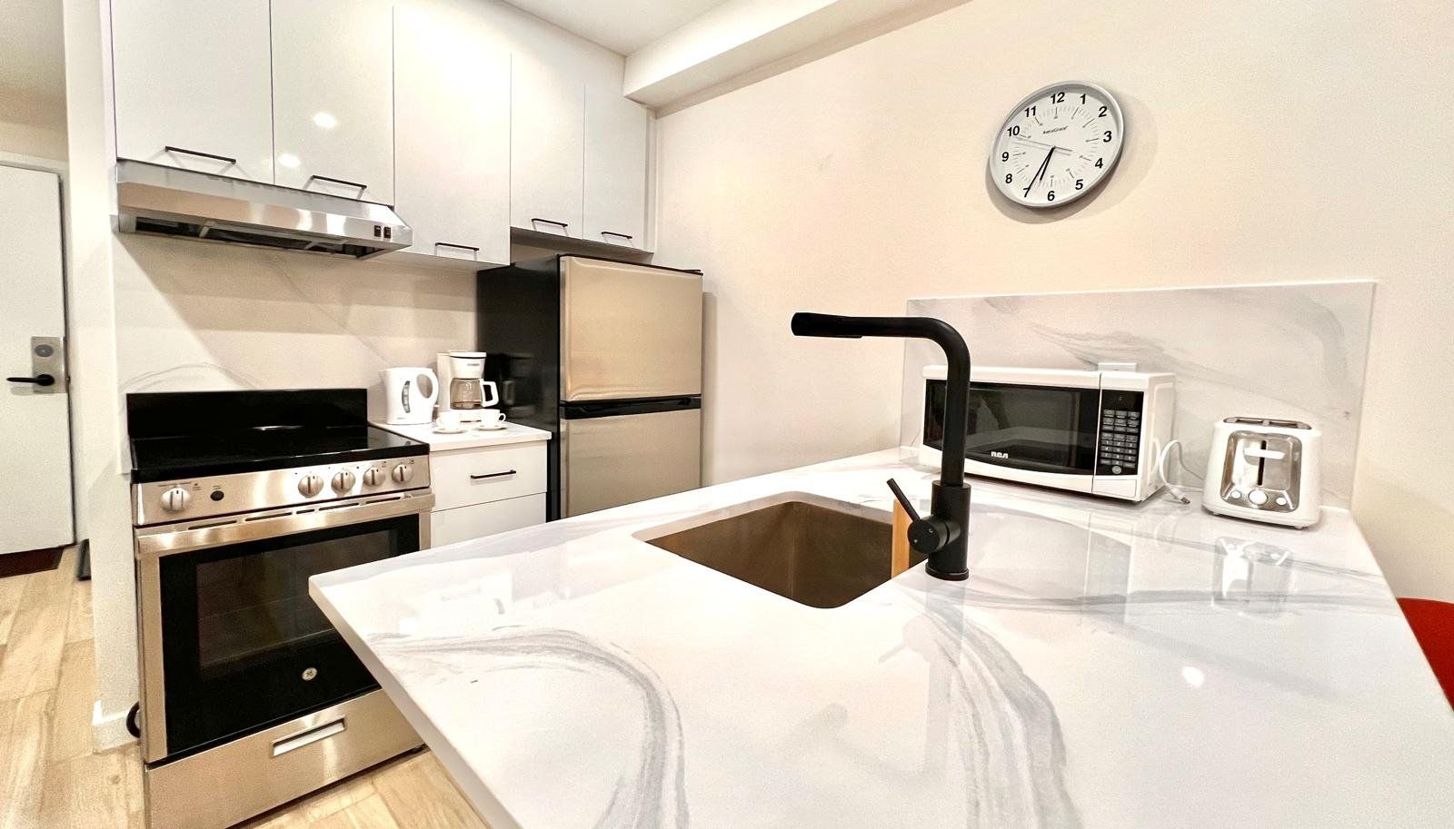 Una cocina moderna con electrodomésticos de acero inoxidable, una encimera blanca y un reloj montado en la pared.