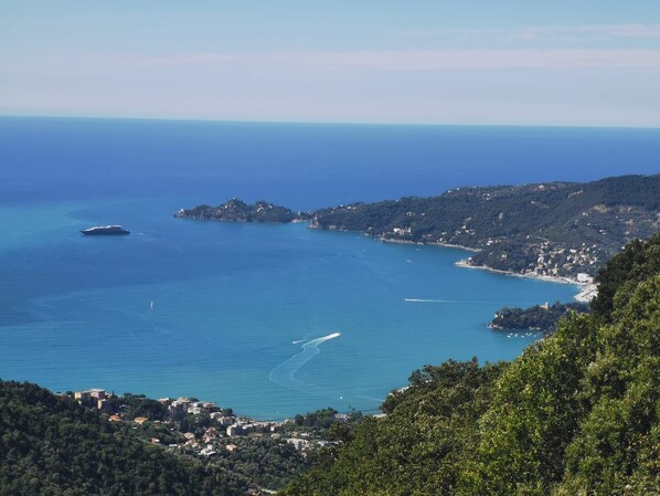 Paisagem costeira com vista clara para o mar, um barco e uma cidade nas colinas.