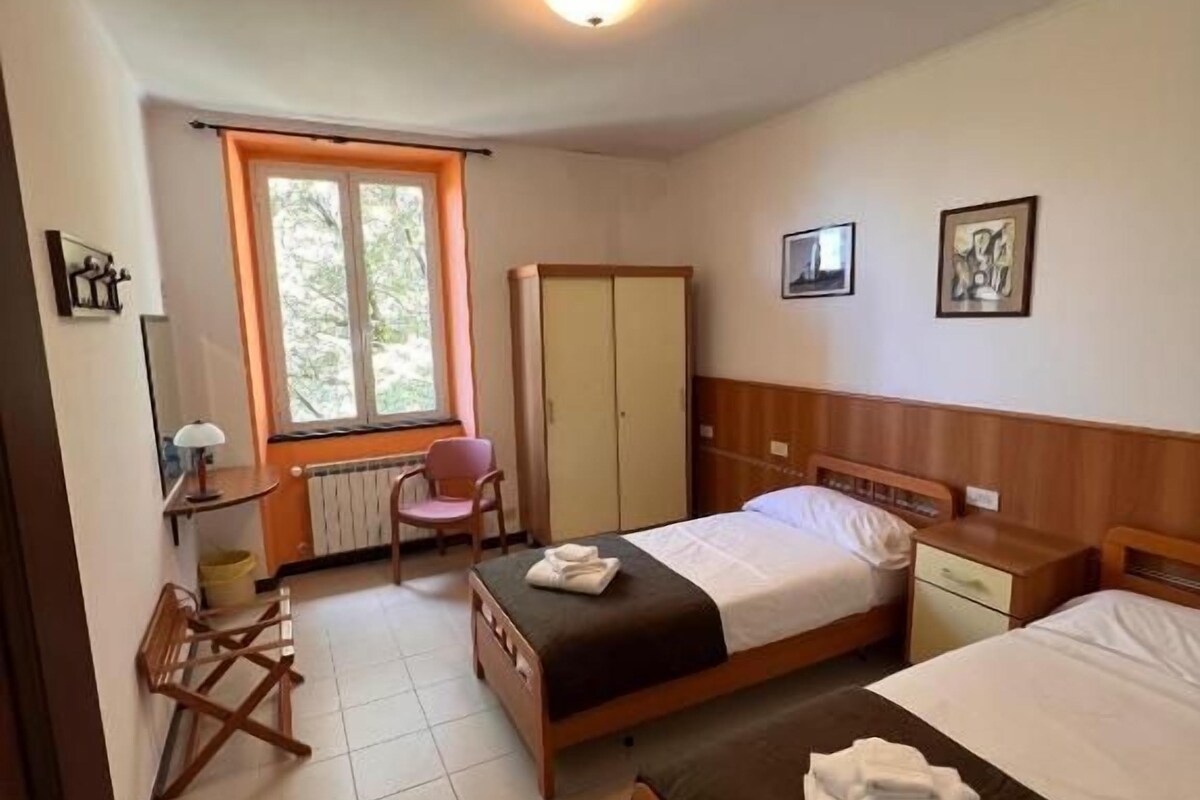 Une chambre d’hôtel avec deux lits, un bureau, une chaise et une fenêtre.