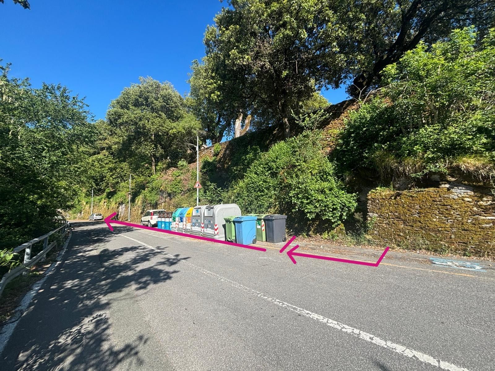 A road with a curve, trees, and parked vehicles.