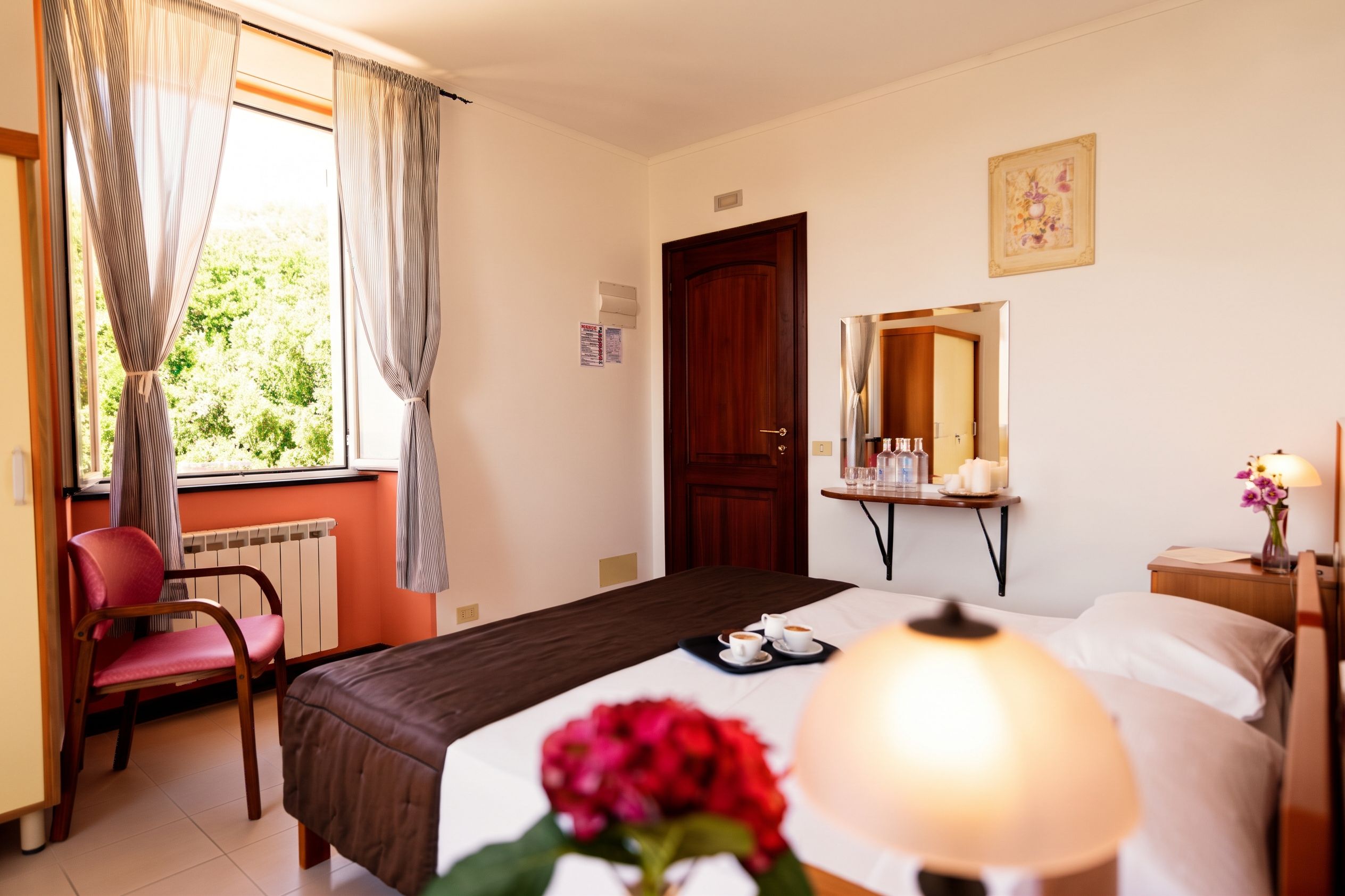 Habitación de hotel con una cama, una silla, una mesa con lámpara y una ventana con cortinas.