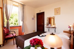 Quarto de hotel com cama, uma cadeira, mesa com abajur e janela com cortinas.