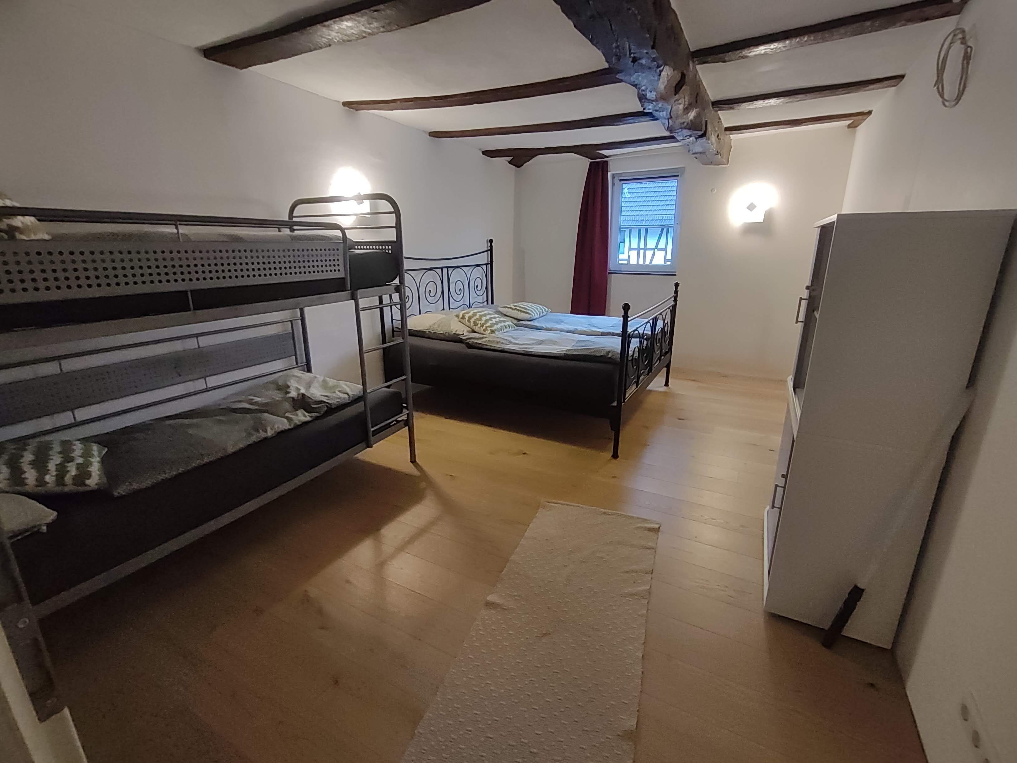 A room with bunk beds, a single bed, a refrigerator, and a window with curtains.