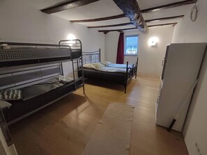 Une chambre avec des lits superposés, un lit simple, un réfrigérateur et une fenêtre avec des rideaux.