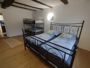 Un lit simple avec un cadre en métal et une tête de lit ornée d’un motif décoratif. Une lampe est fixée au mur au-dessus du lit.