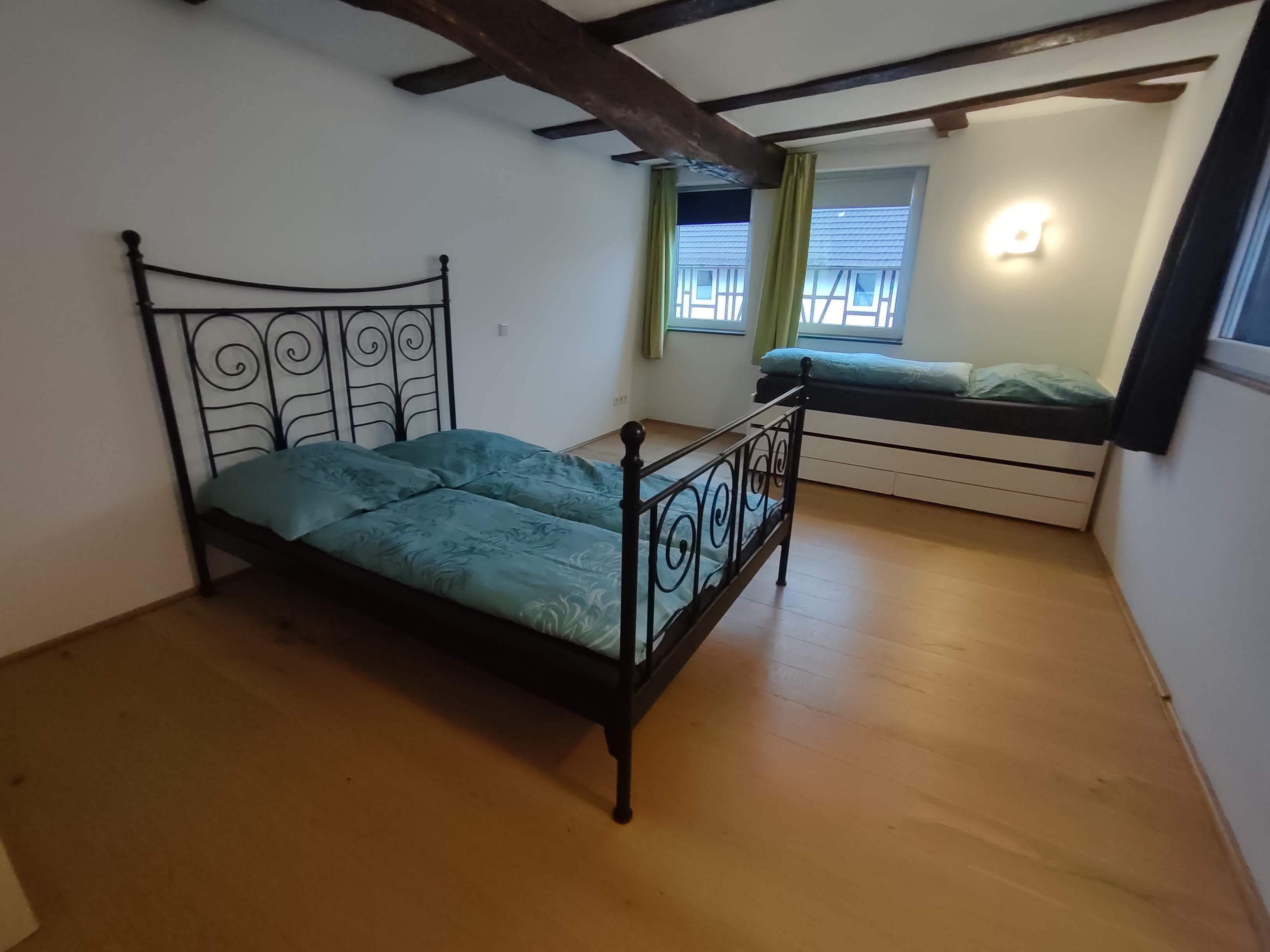 A bedroom with a single bed, a window with curtains, and a ceiling with exposed beams.