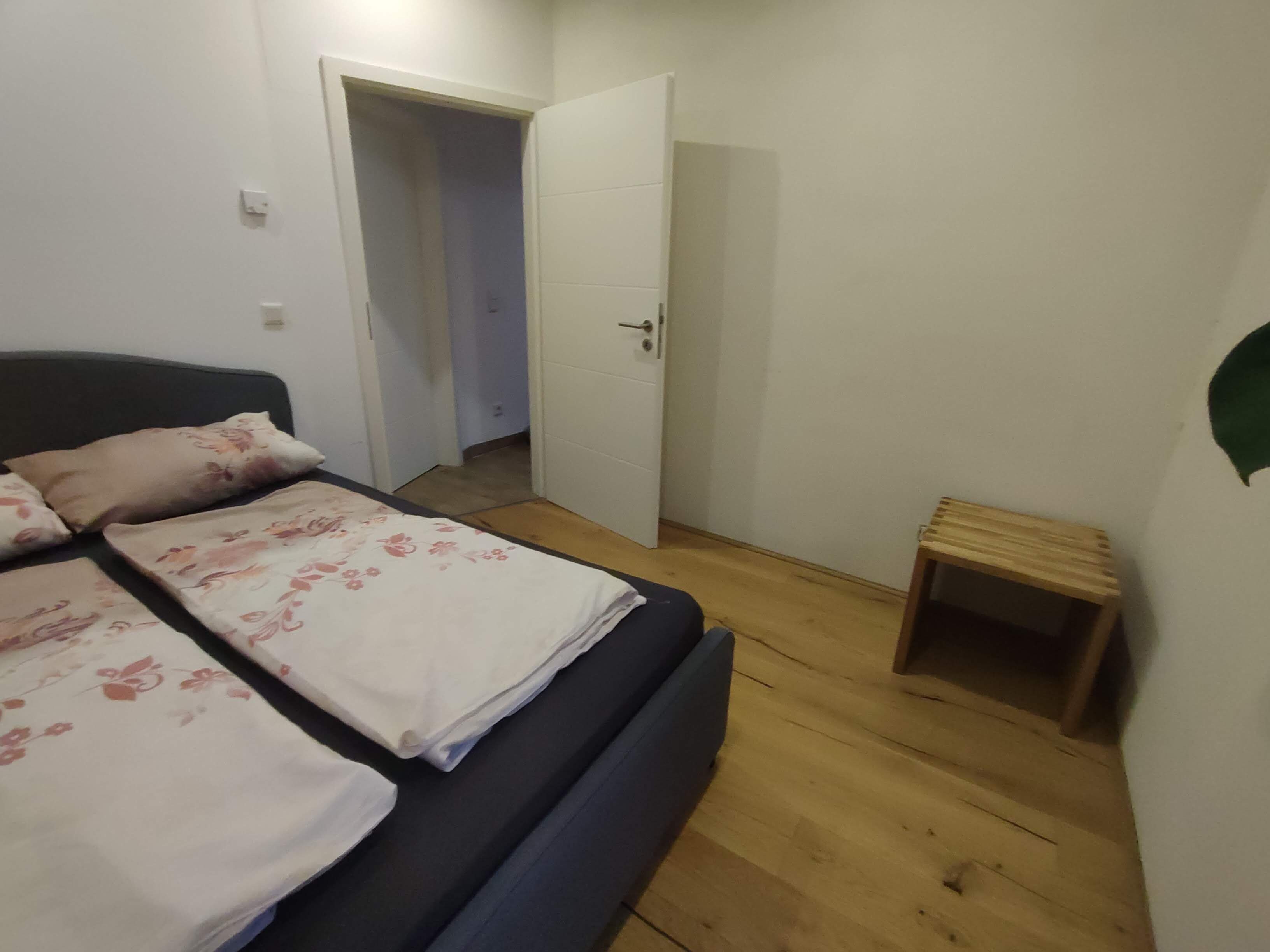 A bedroom with a bed, a door, and a small wooden stool.